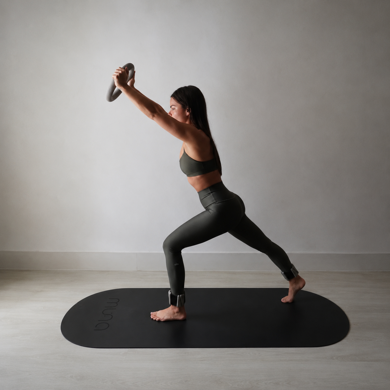 Woman practicing yoga on a Muna oval yoga mat, in a strong pose with weights, showcasing comfort and grip.