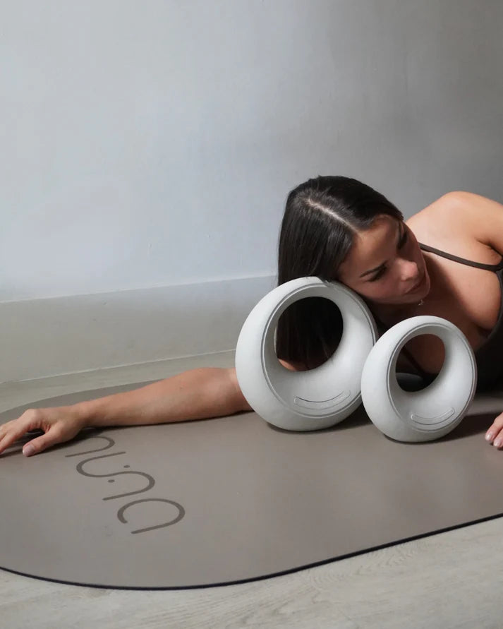 Model using Muna equipment on a yoga mat, showcasing versatile strength training tools including kettlebells.
