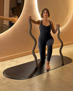 A woman demonstrating exercises on a long dumbbell beam in a stylish fitness studio.