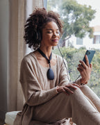 Woman using Sensate vagus nerve toning device while listening to music on her phone at home.