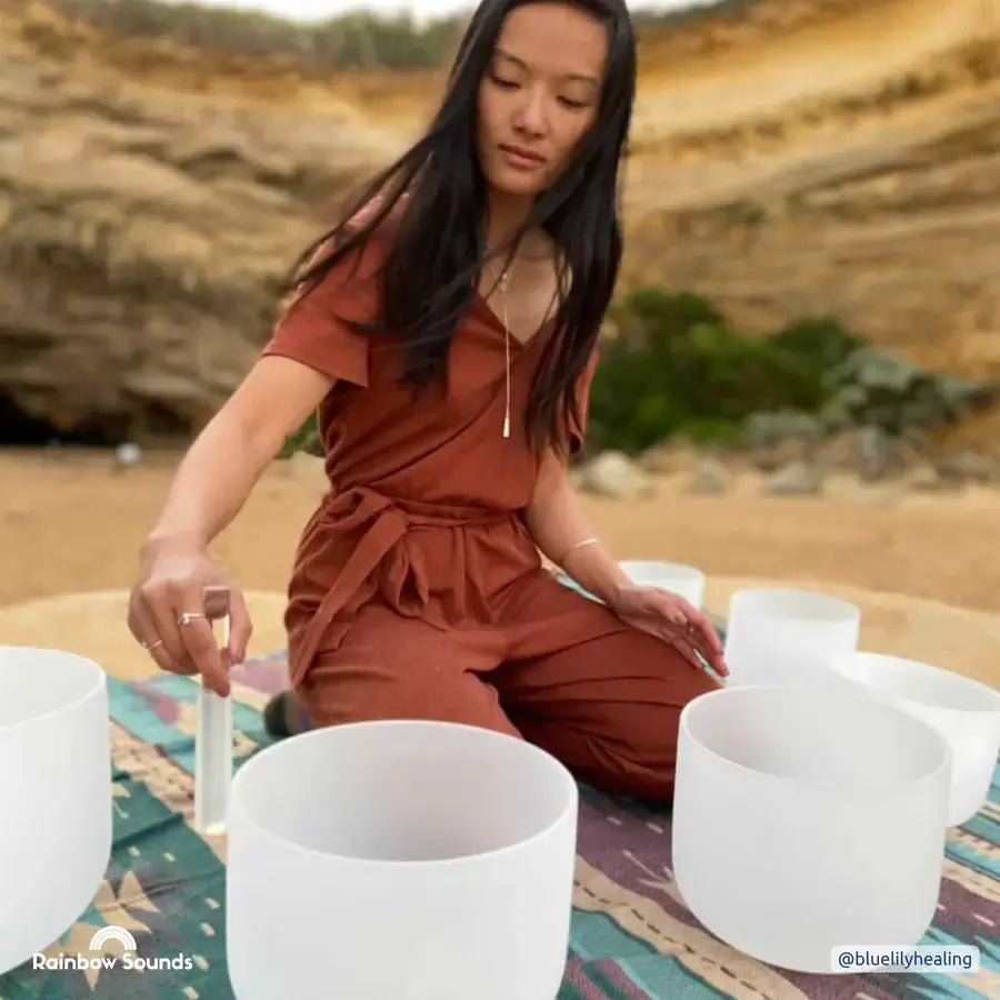 woman using crystal bowl for meditation with crystal bowls on a beach