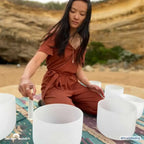 woman using crystal bowl for meditation with crystal bowls on a beach