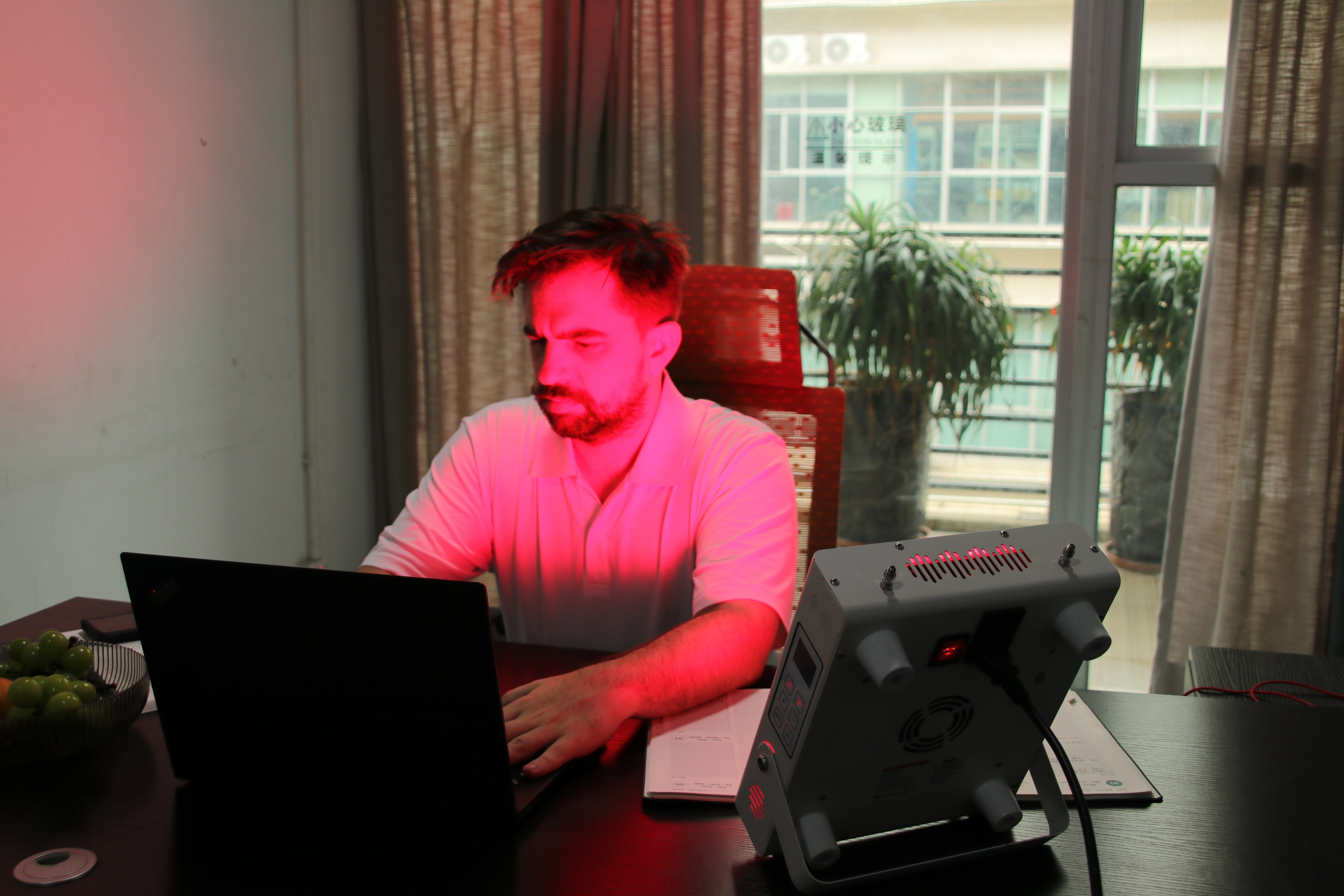 Red Light Therapy Panel in use by a man working on a laptop at home, soft red light ambiance.