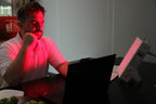 Man using Red Light Therapy Panel while working on a laptop at a desk with a plate of grapes.