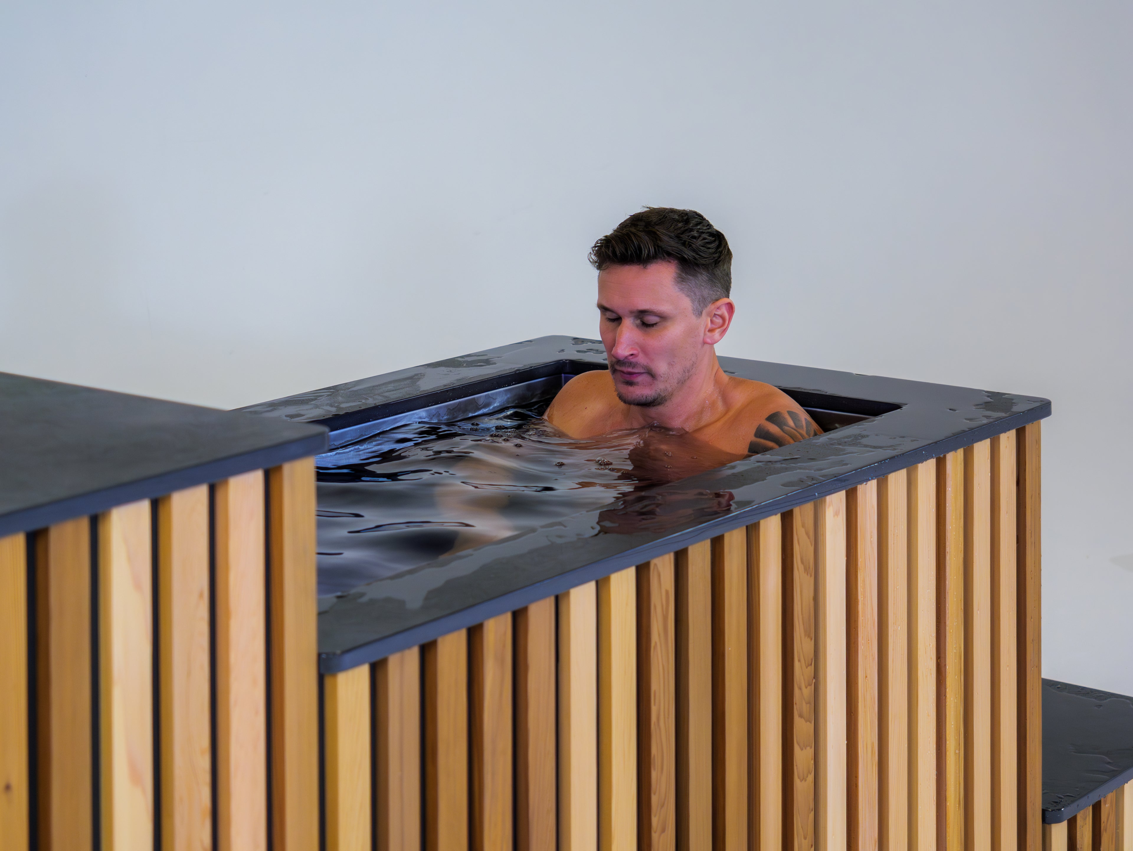 Man sitting in a small pool with wooden sides and a white background